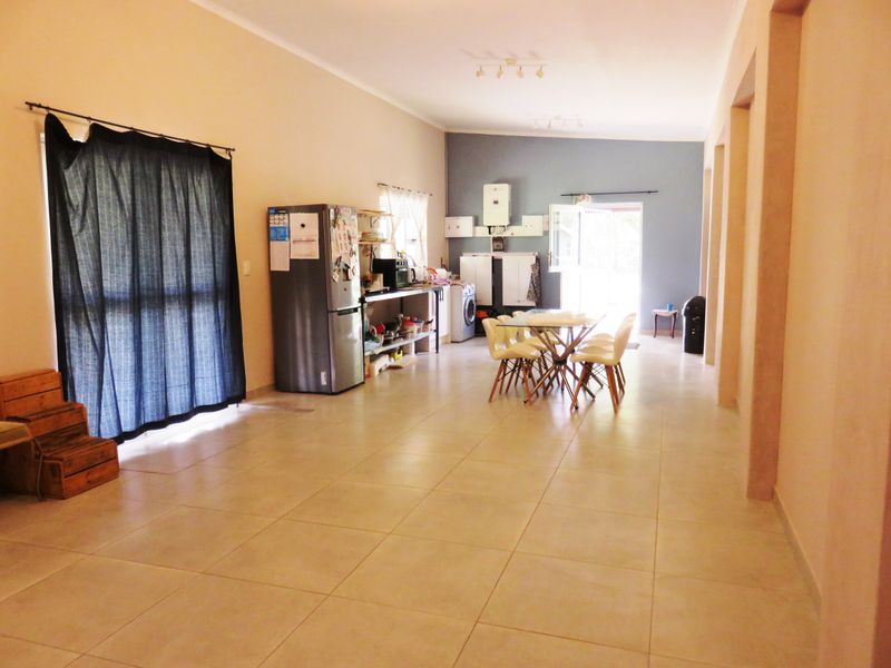 Spacious open-plan living and dining area featuring neutral tiled flooring and functional utility space with built-in shelving and gas water heater.