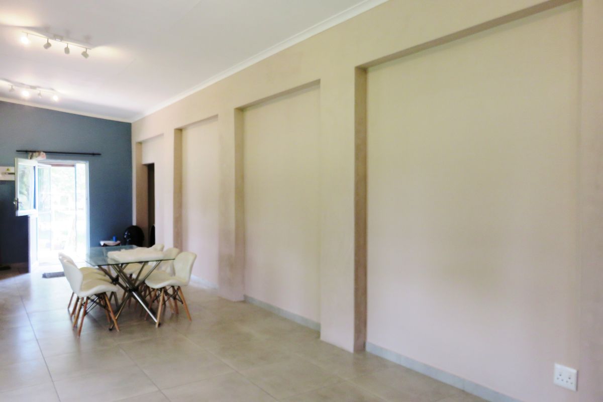 Spacious living area featuring large recessed wall niches, neutral tiled flooring, and modern track lighting, leading to an outdoor access point.