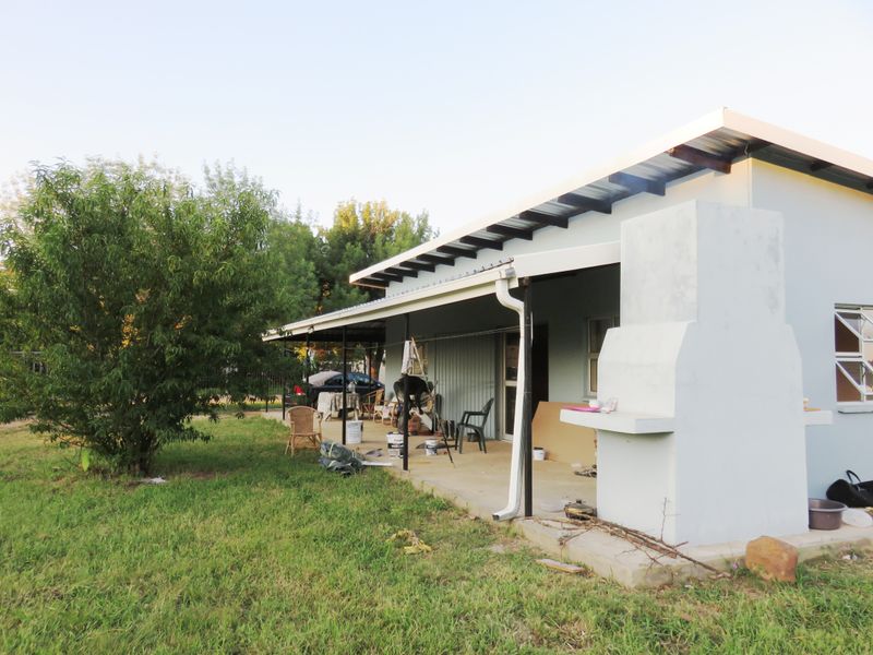 Covered outdoor patio area featuring a built-in braai, concrete flooring, and metal roofing, providing a functional space for outdoor entertaining.