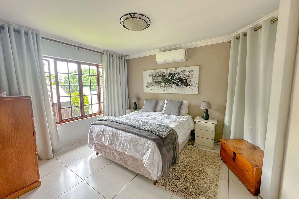 A well-maintained bedroom featuring tiled flooring, crown molding, a wall-mounted air conditioning unit, and large windows providing natural light.