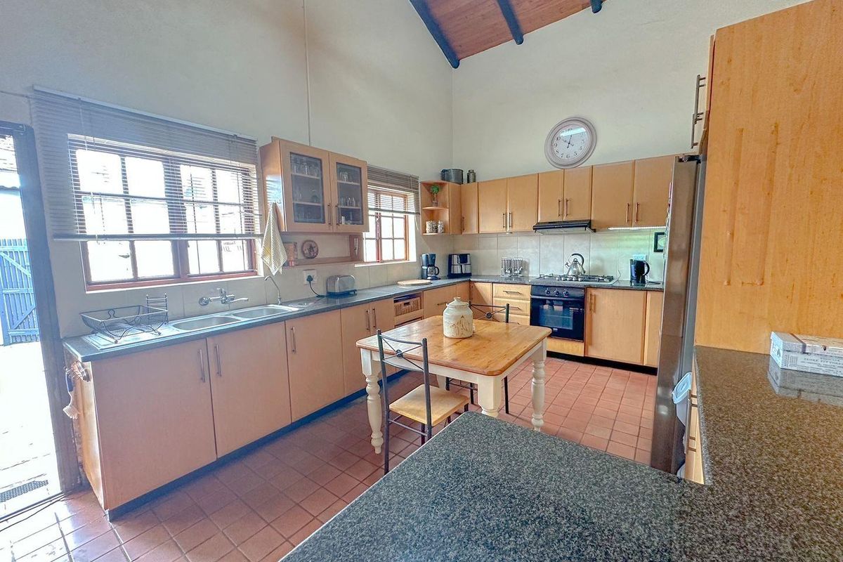 Spacious kitchen featuring light wood cabinetry, granite countertops, a built-in oven and hob, and a high vaulted ceiling with exposed timber beams.