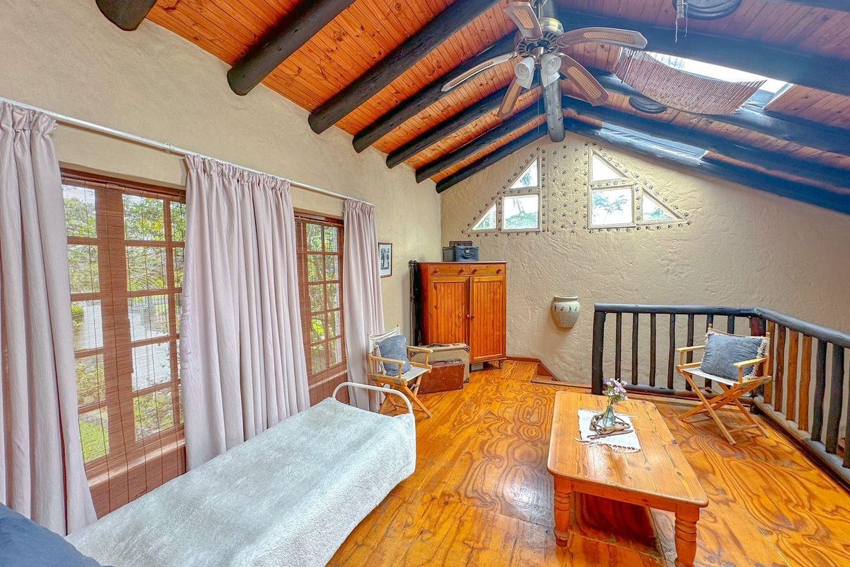 A rustic loft living area featuring exposed timber beams, vaulted ceilings, wooden flooring, and triangular feature windows overlooking the space below.