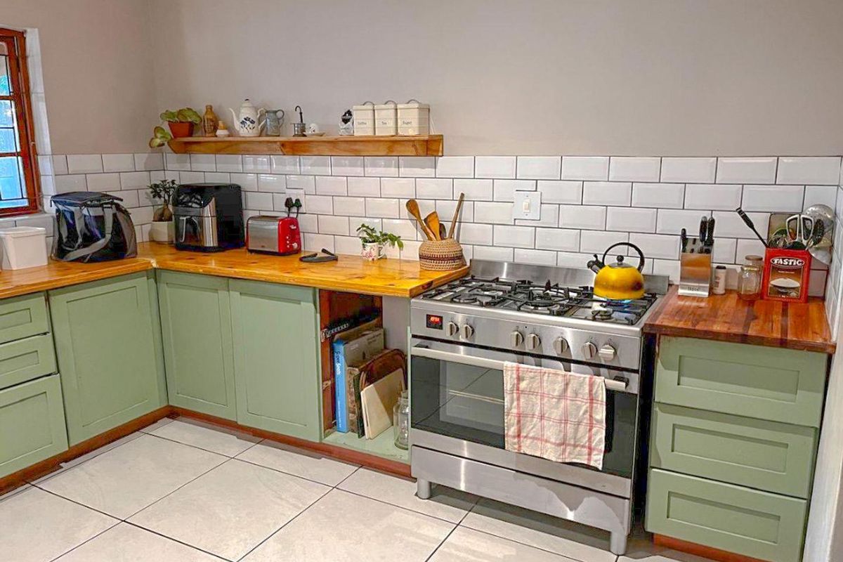 A well-maintained kitchen featuring sage green shaker-style cabinetry, warm wooden countertops, a subway tile backsplash, and a stainless steel gas stove.