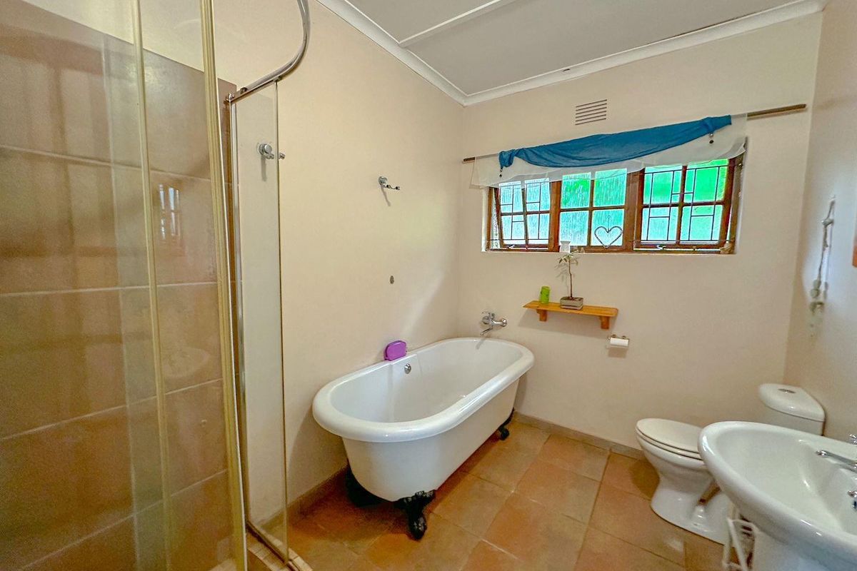 A functional bathroom featuring a classic freestanding bathtub, a separate glass-enclosed shower, a pedestal sink, and a toilet with tiled flooring.