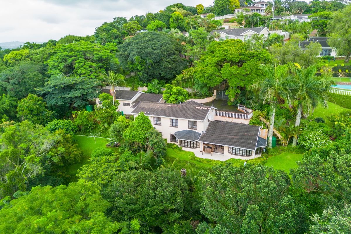 Aerial view of a residential property nestled in a lush, green landscape with a tiled roof and expansive garden area.