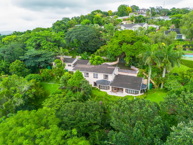 Aerial view of a residential property nestled in a lush, green landscape with a tiled roof and expansive garden area.