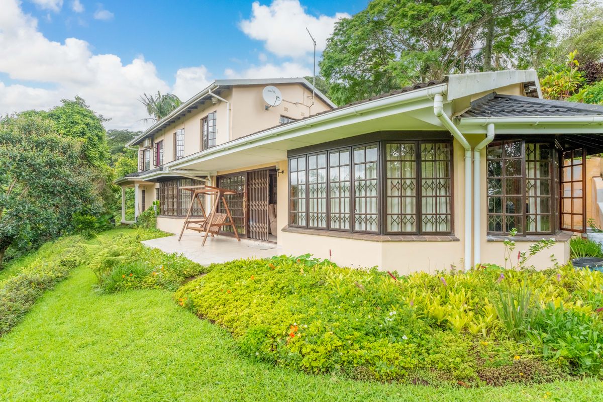 Rear view of the house featuring a covered patio, bay windows with security bars, and a well-maintained garden area.