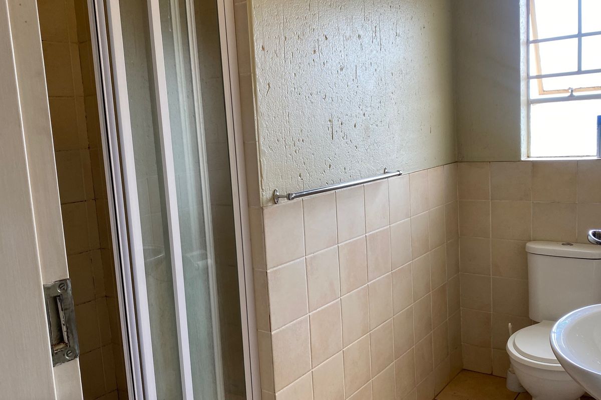 A functional bathroom featuring a shower enclosure, toilet, and washbasin with neutral wall and floor tiling.