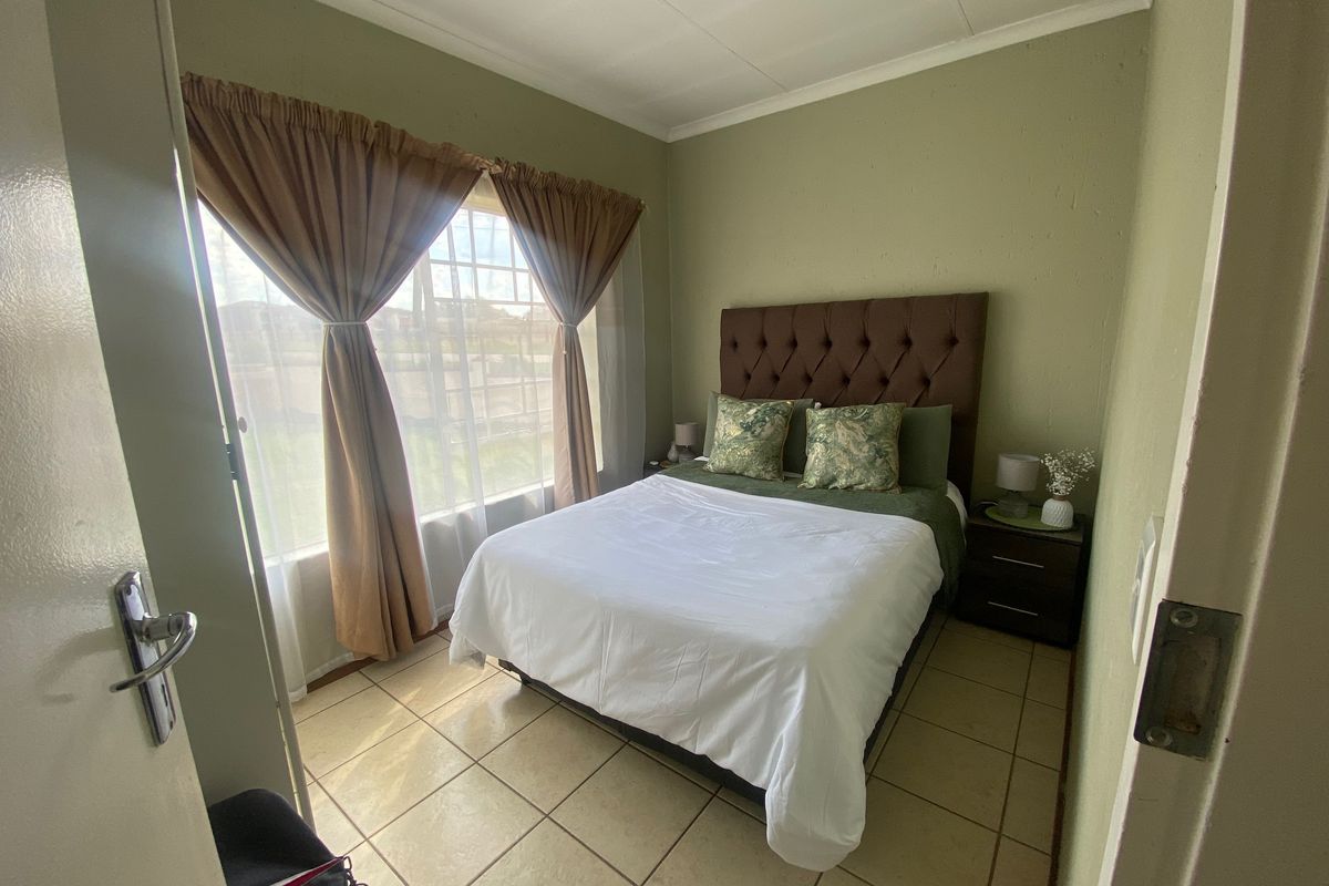 A compact bedroom featuring tiled flooring and a window with security bars, providing a functional and well-lit sleeping space.