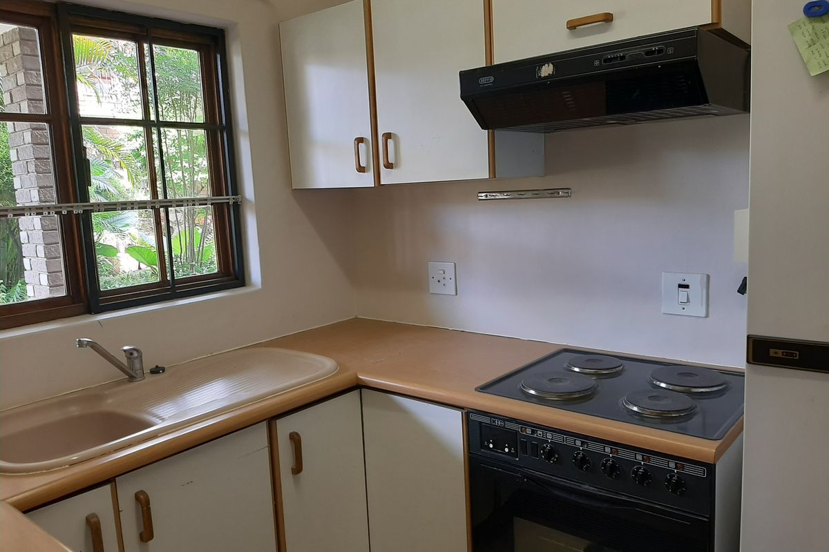 A functional kitchen featuring laminate countertops, built-in cabinetry, an electric stove with extractor fan, and a sink overlooking the garden.