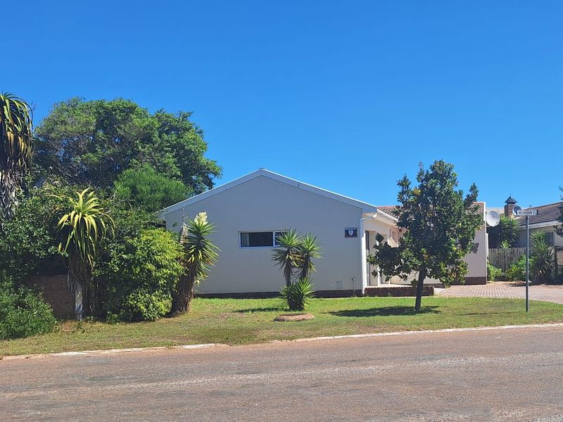 Front view of a residential house featuring a paved driveway, established garden, and lawn area from the street perspective.
