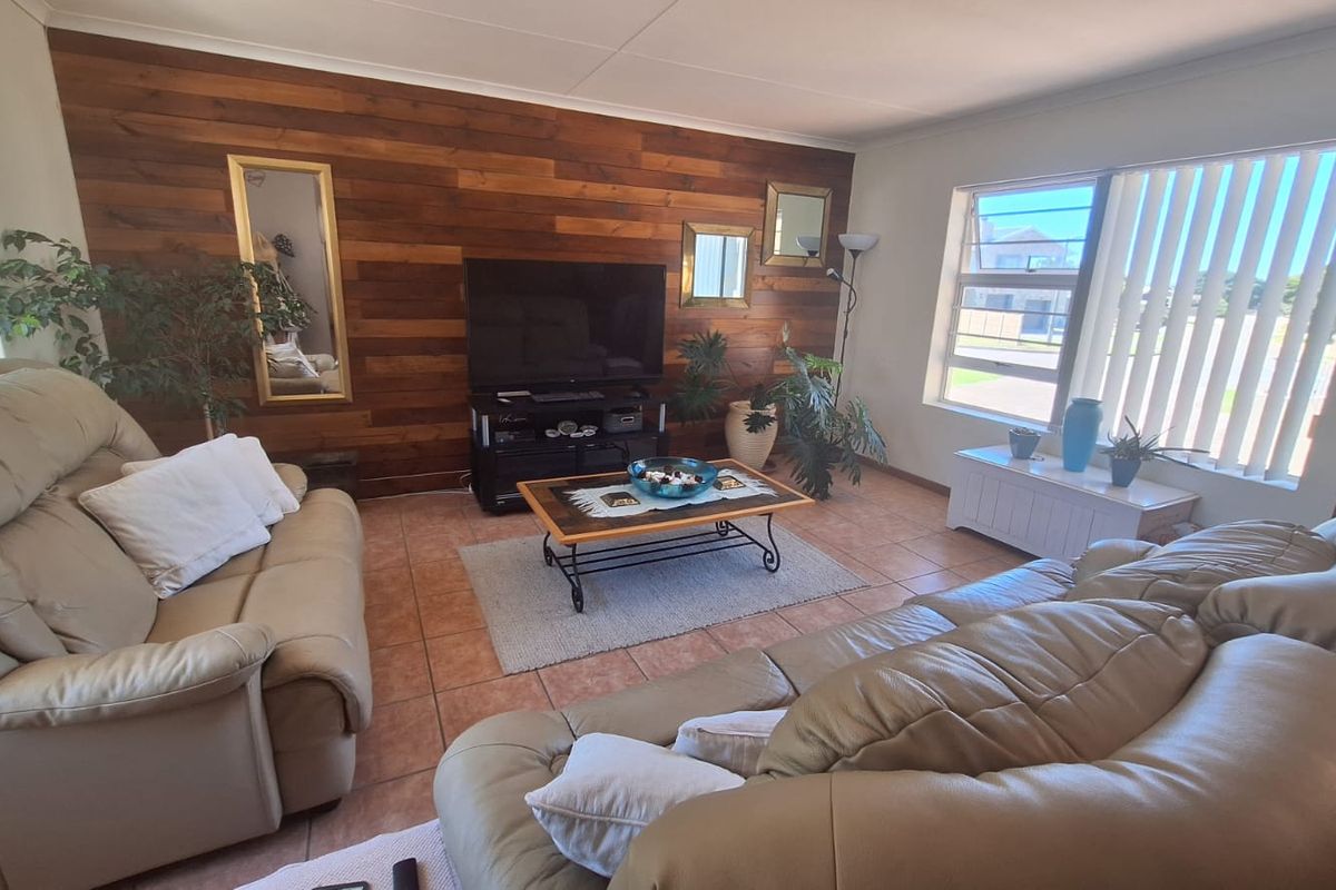 A living room featuring a wood panel accent wall, ceramic tile flooring, and large windows with vertical blinds, offering a comfortable and functional living space.