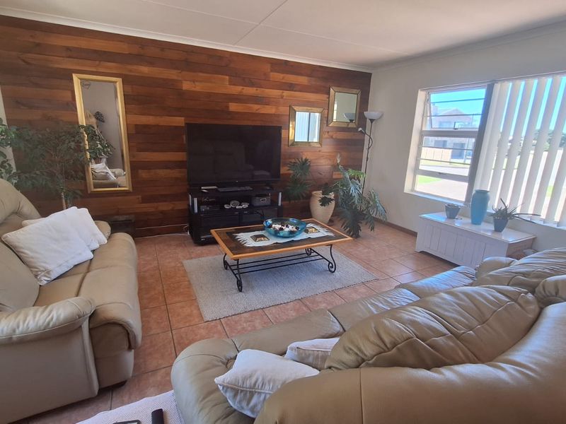 A living room featuring a wood panel accent wall, ceramic tile flooring, and large windows with vertical blinds, offering a comfortable and functional living space.