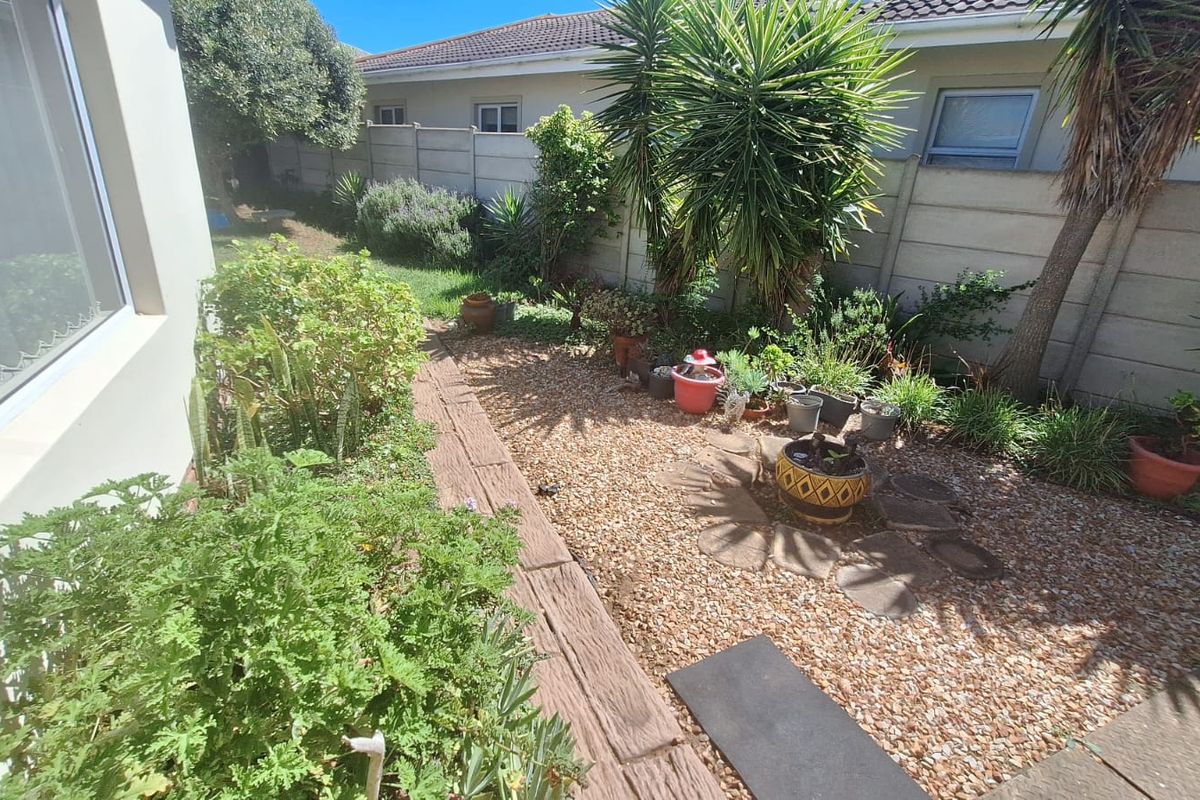 A low-maintenance rear garden area featuring gravel landscaping, established greenery, and a secure precast concrete boundary wall.