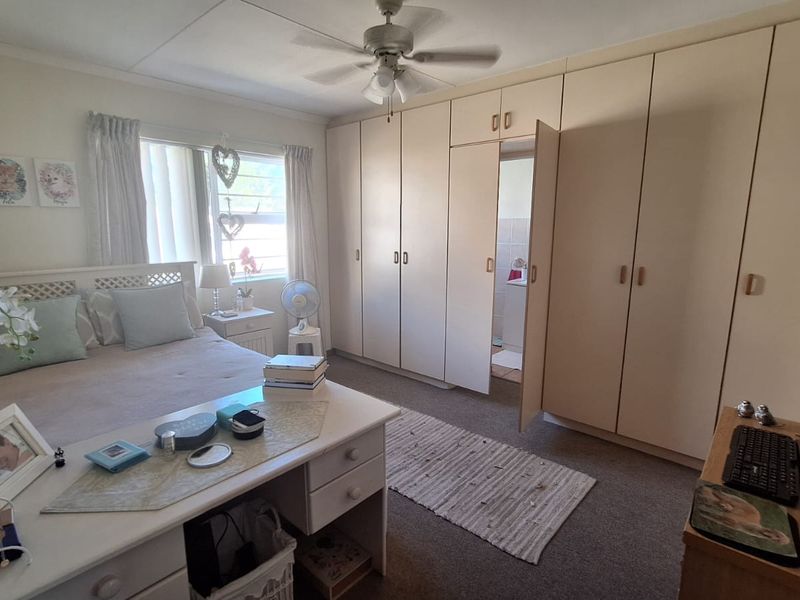 A bedroom featuring extensive built-in cupboards, a ceiling fan, and natural light from the window.