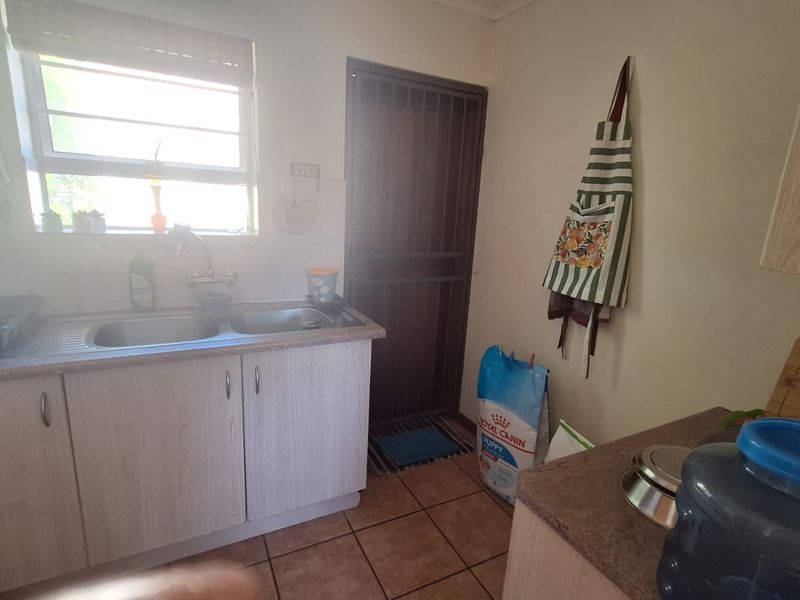 A functional scullery area featuring double bowl stainless steel sink, laminate cabinetry, tiled flooring, and a secure exterior door.