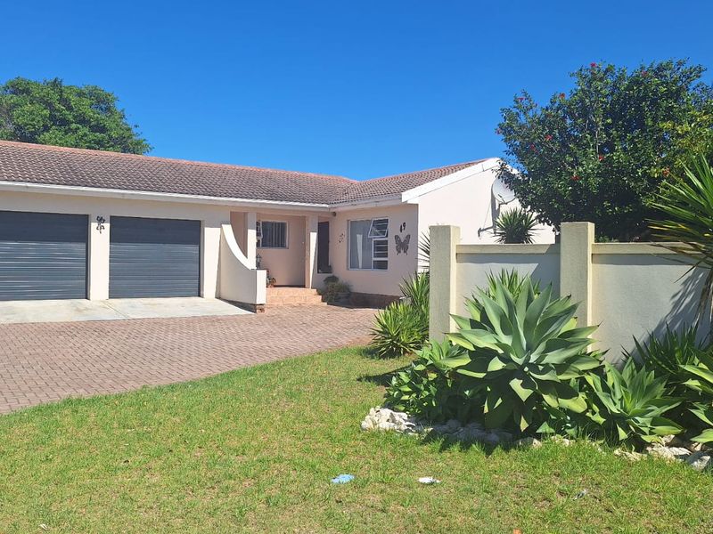 Front view of a single-story residential property featuring a double garage, paved driveway, and a well-maintained boundary wall with established garden landscaping.