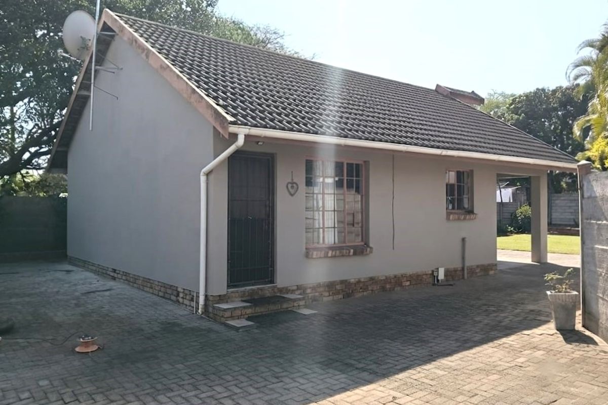 Rear exterior view of the flat featuring a tiled roof, brick paved driveway, and secure entrance with security gate.