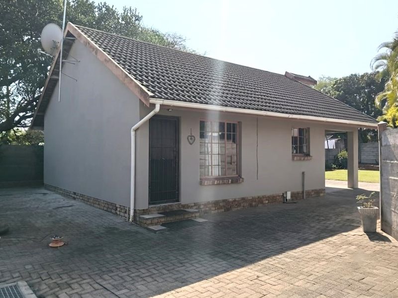 Rear exterior view of the flat featuring a tiled roof, brick paved driveway, and secure entrance with security gate.