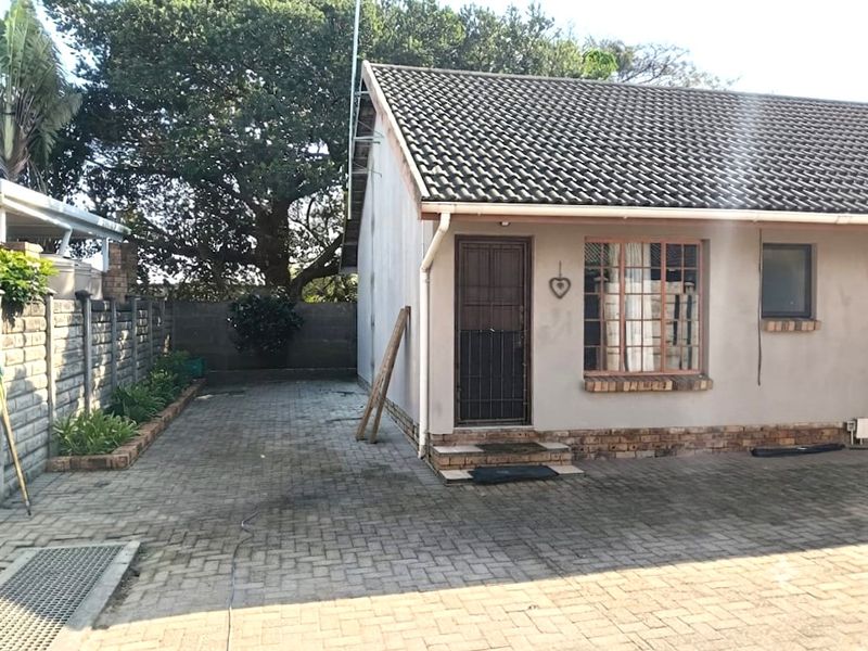 Front exterior view of the flat featuring a tiled roof, brick paved driveway, and secure entrance with a security gate.