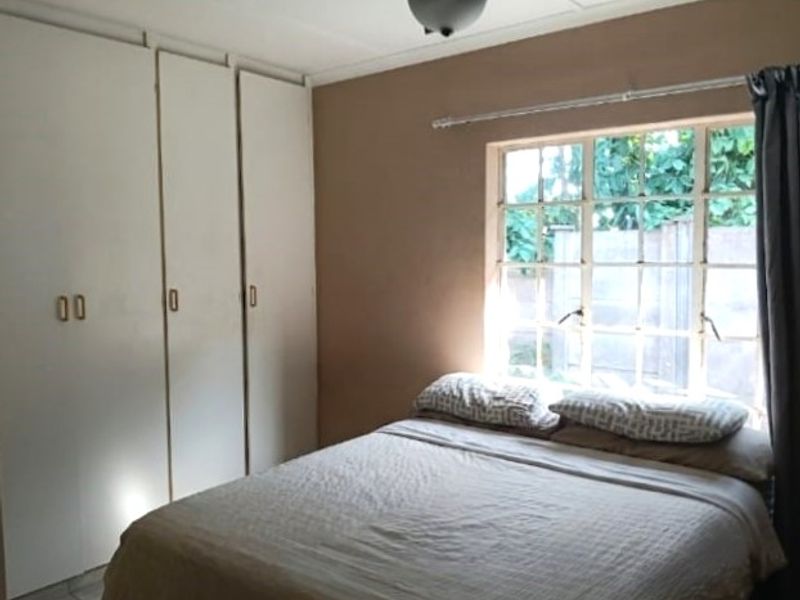 A bedroom featuring built-in cupboards and a steel-framed window, providing natural light and storage space.