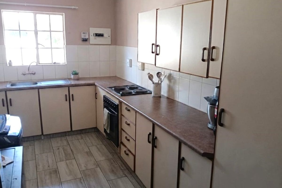 A functional kitchen featuring laminate countertops, built-in cabinetry, an electric hob, and a stainless steel sink with tiled backsplash and flooring.