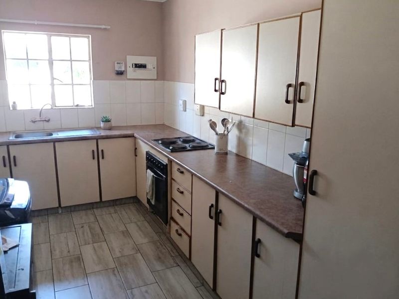 A functional kitchen featuring laminate countertops, built-in cabinetry, an electric hob, and a stainless steel sink with tiled backsplash and flooring.