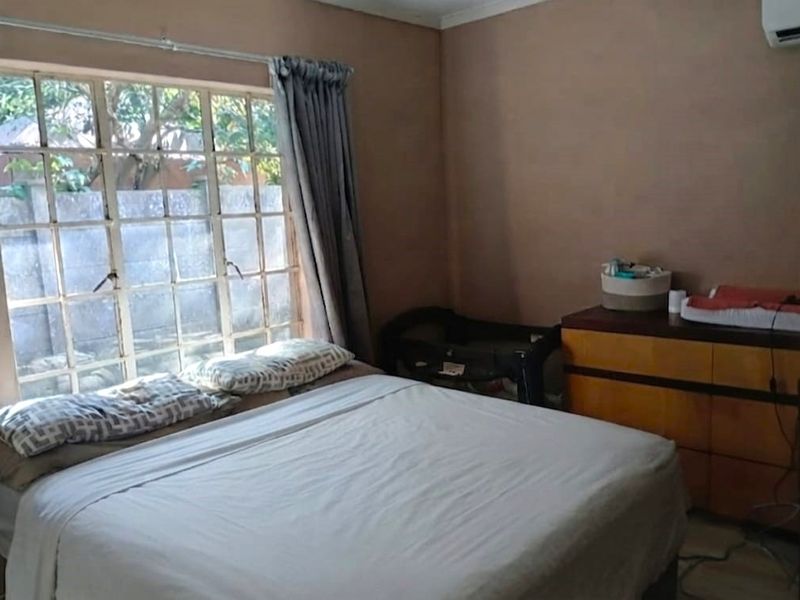 A bedroom featuring a large grid-pane window and a wall-mounted air conditioning unit, providing a functional space with natural light.