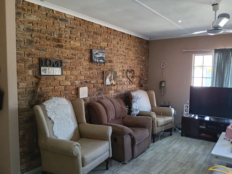 A living room featuring a prominent exposed brick feature wall, tiled flooring, and a ceiling fan, offering a warm and textured living space.