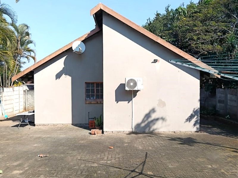 Rear exterior view of the property featuring a paved driveway, exterior wall with an air conditioning unit, and perimeter boundary wall.