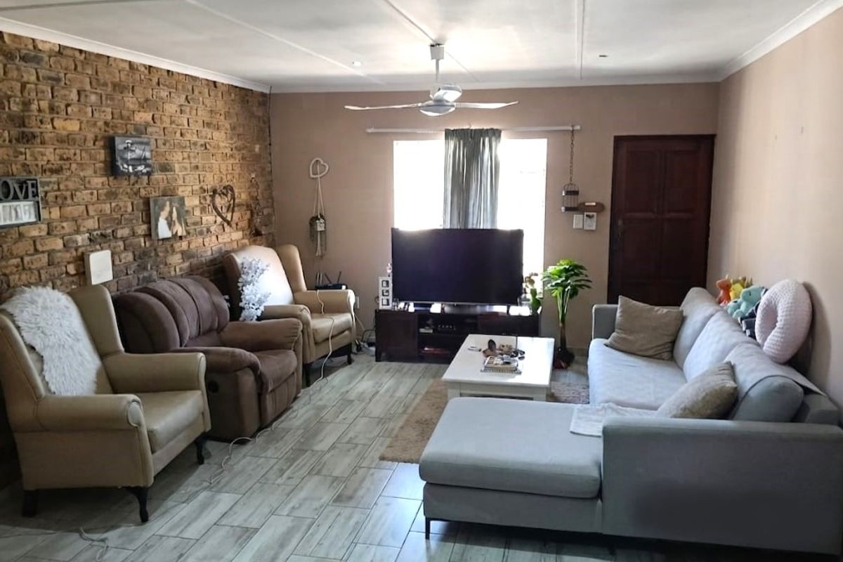 A comfortable living room featuring an exposed brick accent wall, modern tiled flooring, and a ceiling fan, offering a warm and inviting atmosphere.