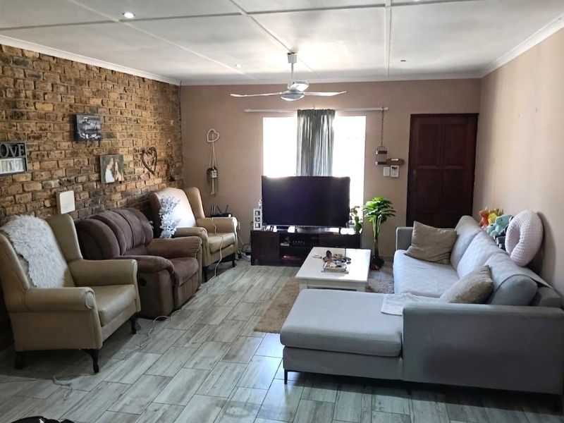 A comfortable living room featuring an exposed brick accent wall, modern tiled flooring, and a ceiling fan, offering a warm and inviting atmosphere.