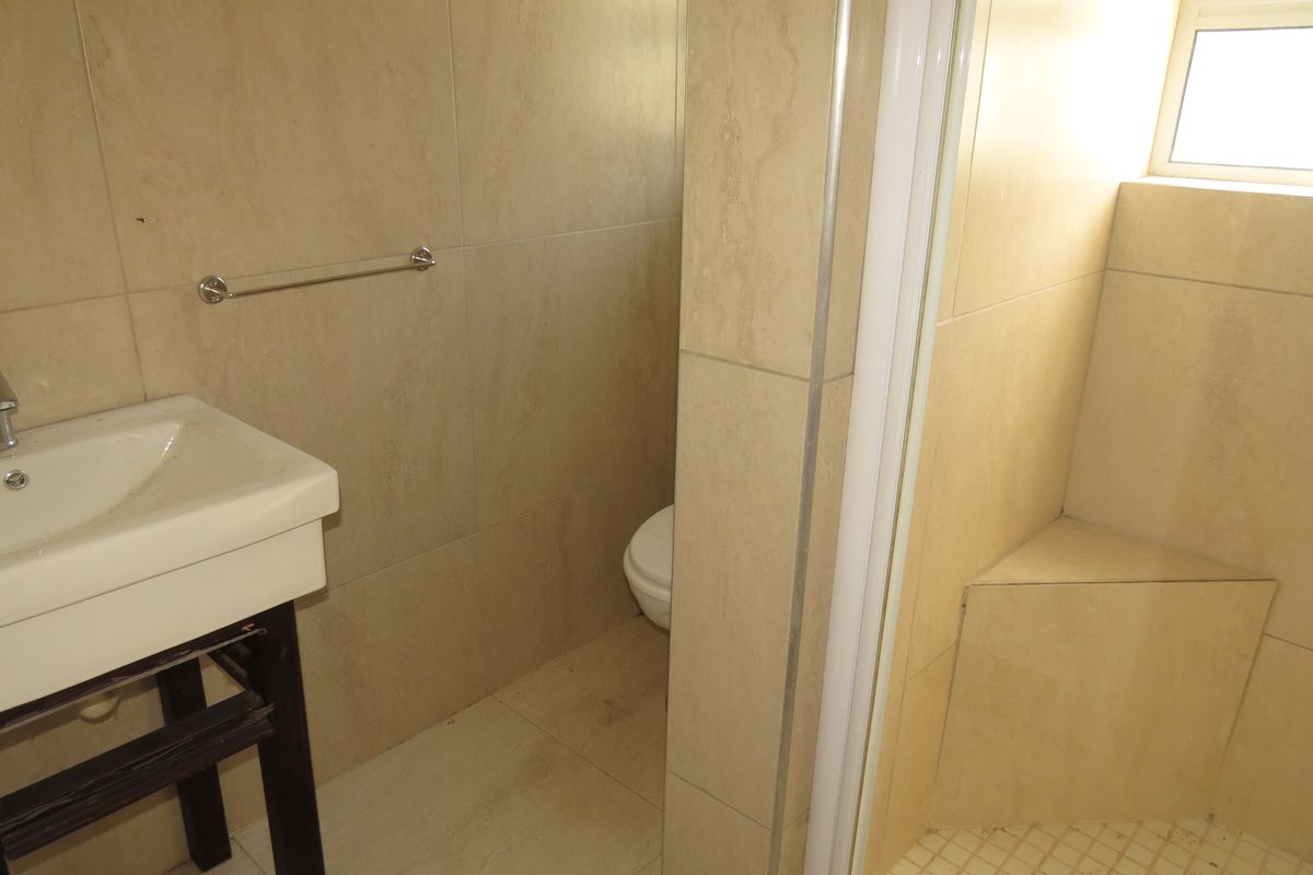 A functional bathroom featuring a wall-mounted basin, a tiled shower enclosure with a built-in seat, and a separate toilet area.