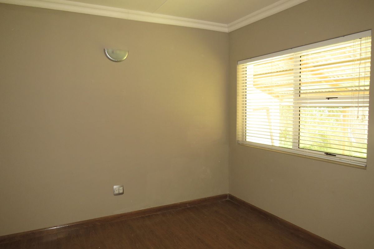 An empty bedroom featuring laminate flooring, neutral wall tones, and a window fitted with venetian blinds.