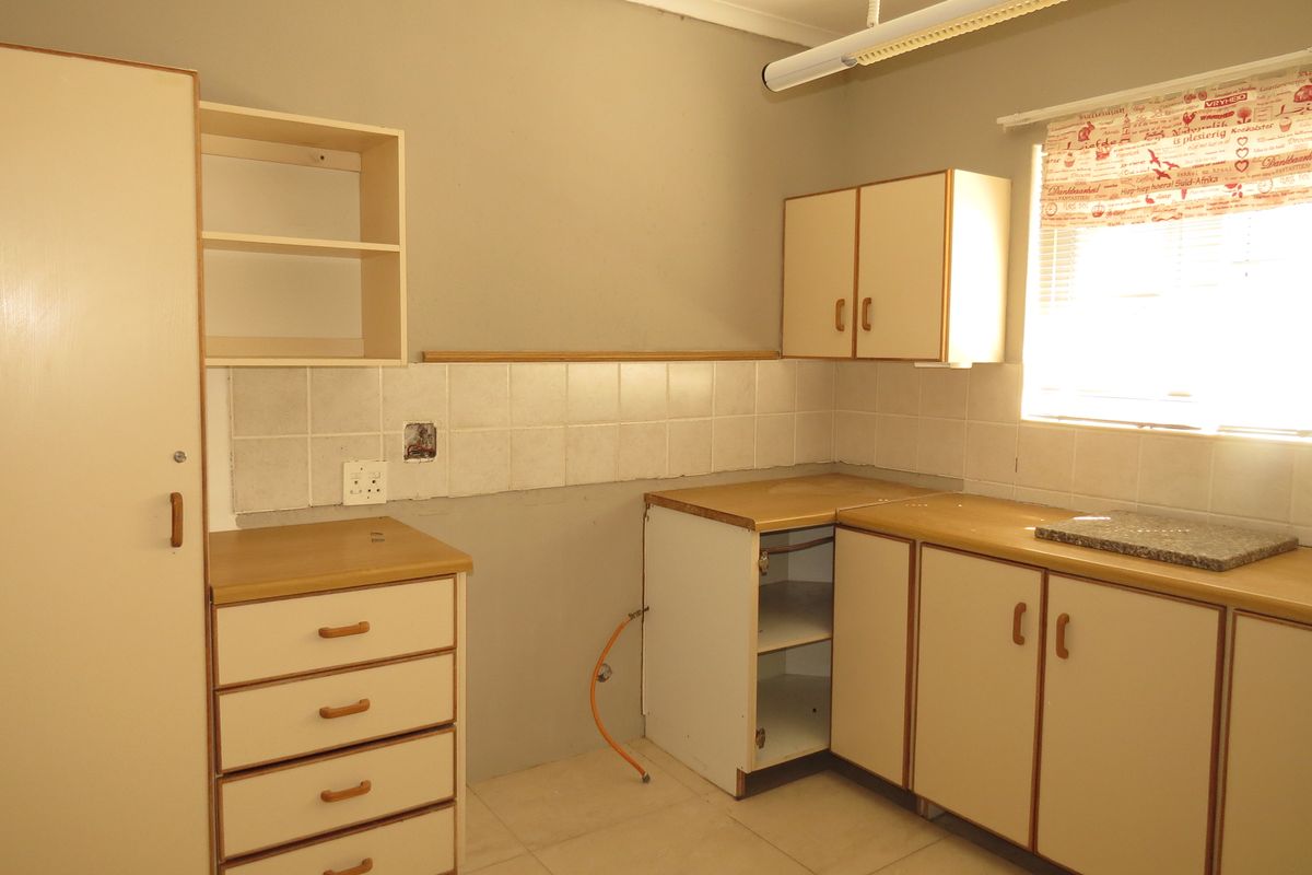 A dated kitchen area featuring built-in cabinetry, laminate countertops, and tiled backsplash, currently vacant and requiring cosmetic updates.
