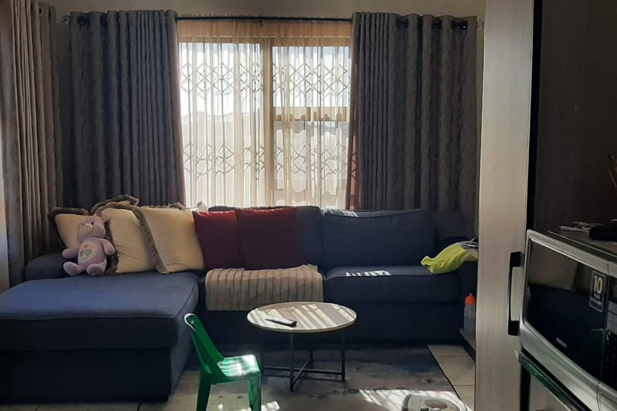 A comfortable living room area featuring tiled flooring and a large sliding glass door with security gate, providing natural light to the space.