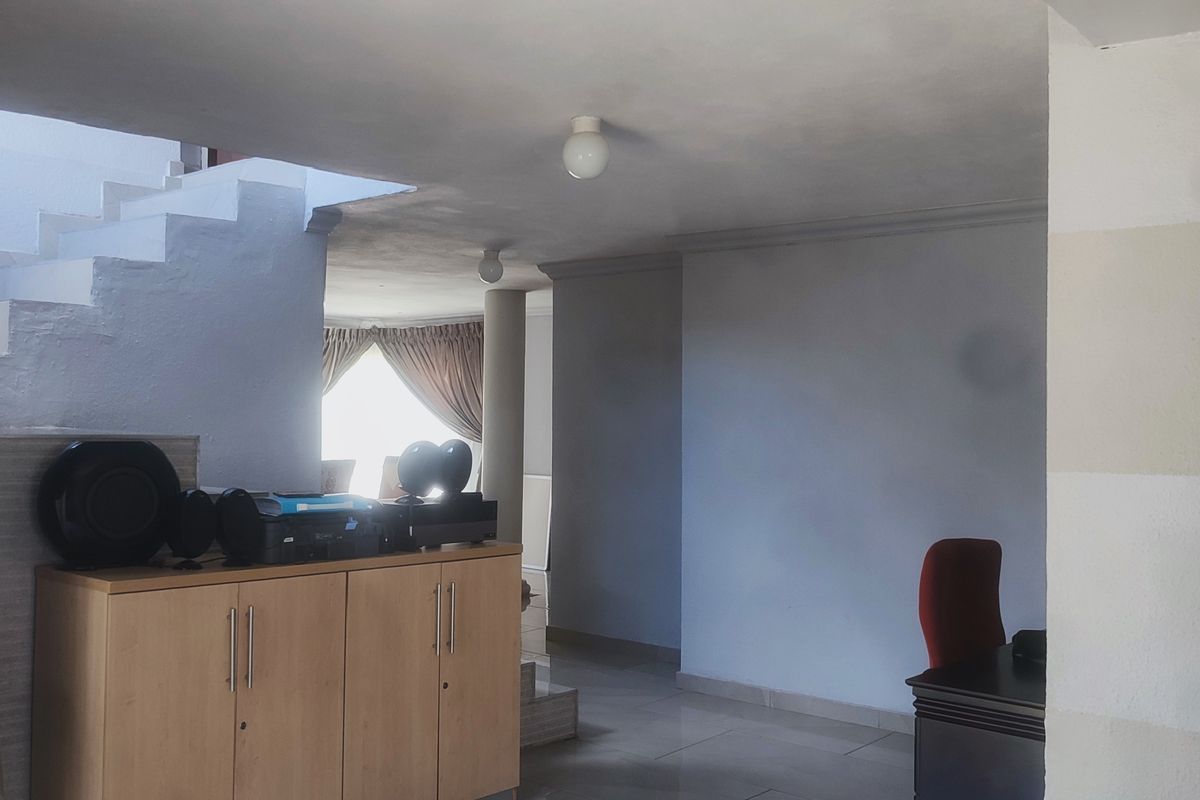 An open-plan living area featuring tiled flooring, a central support column, and a staircase leading to the upper level.