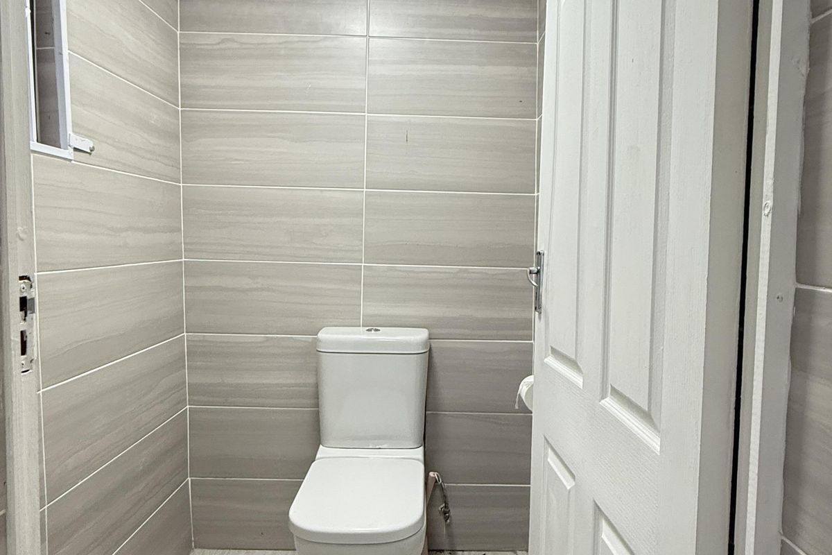 A compact, modern bathroom featuring floor-to-ceiling neutral wall tiles, matching floor tiles, and a white ceramic toilet.
