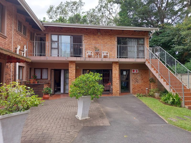 Rear view of a two-story brick retirement village unit featuring a paved courtyard, upper-level balcony, and external metal staircase access.