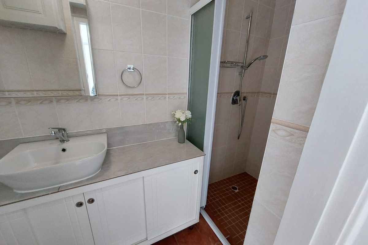 A functional bathroom featuring a vanity cabinet with a basin, a tiled shower enclosure, and neutral wall tiling.