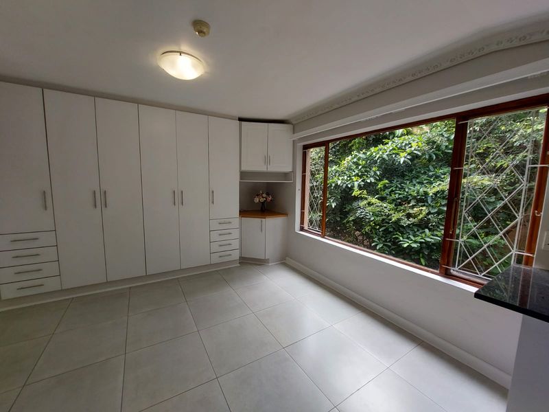 A bright, empty bedroom featuring extensive built-in cabinetry, large windows with security bars, and neutral tiled flooring.