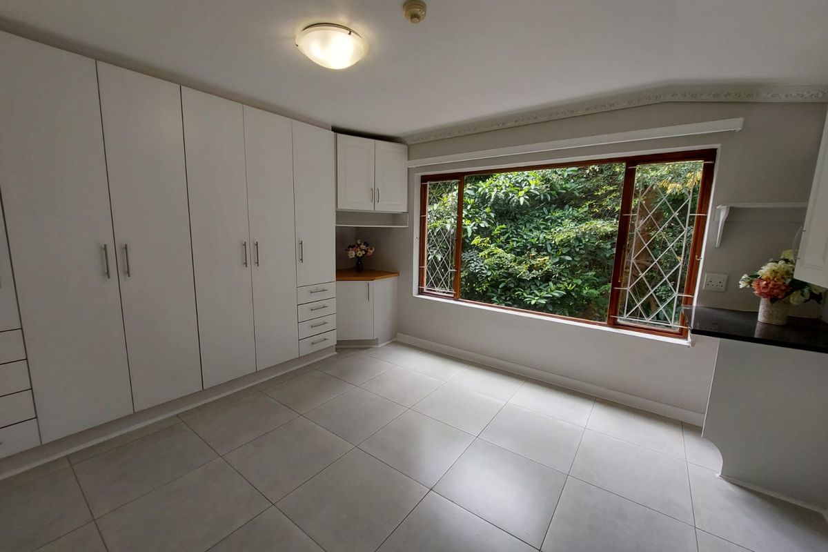 A bright, empty bedroom featuring extensive built-in white cabinetry, large windows with security bars, and neutral tiled flooring.