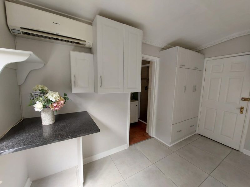 A functional utility space featuring built-in cabinetry, a laminate countertop, split-system air conditioning, and tiled flooring, with direct access to an adjoining room.