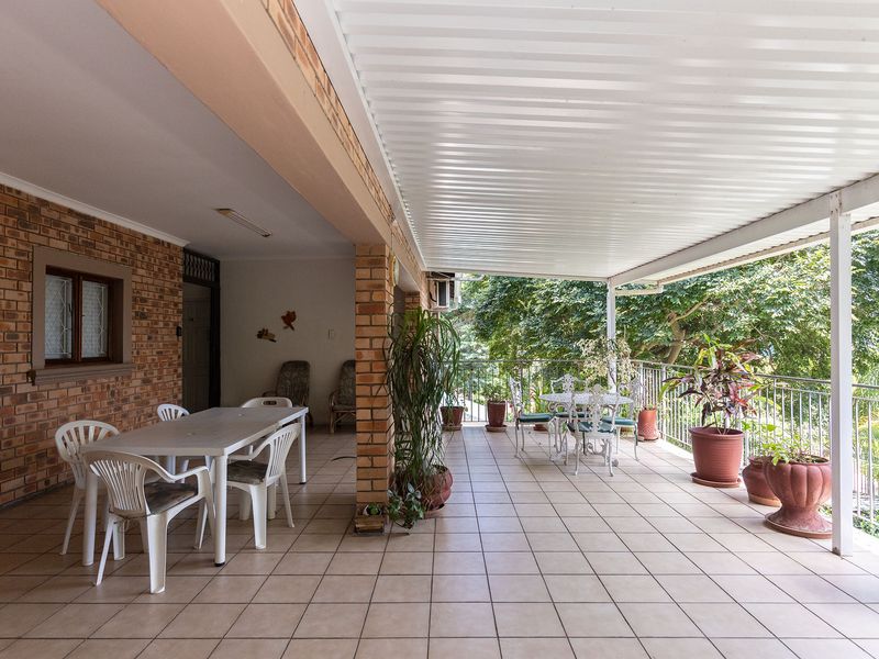 Spacious covered patio featuring tiled flooring, exposed brick walls, and a metal balustrade, offering a functional outdoor entertainment area.
