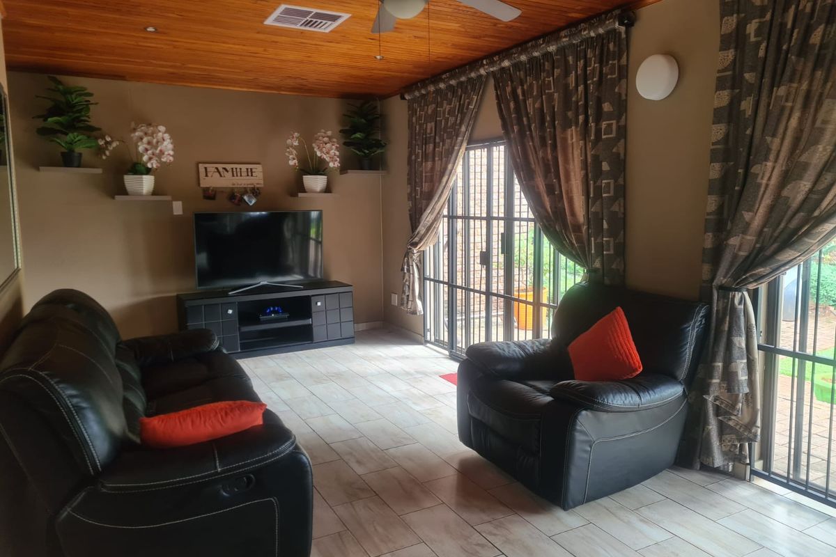 A comfortable living room featuring a warm timber-clad ceiling, ceiling fan, and tiled flooring, with direct access to the outdoor area through sliding glass doors.