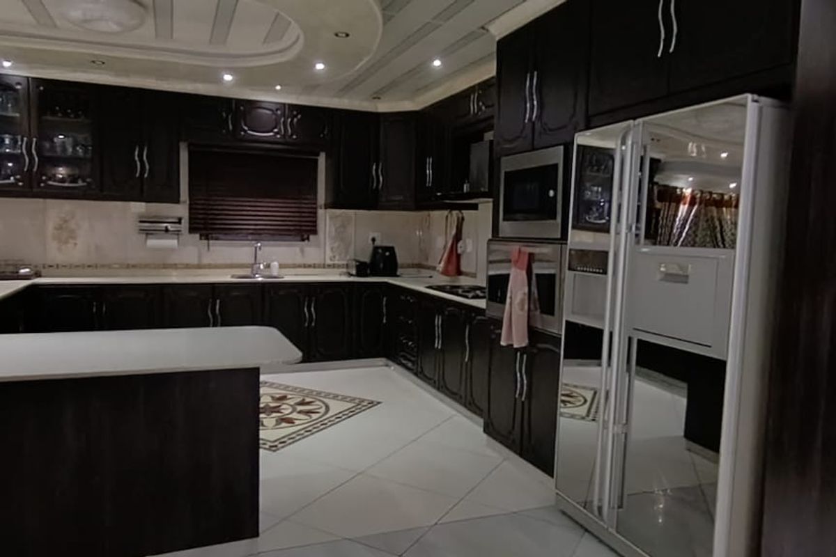 Spacious kitchen featuring dark wood cabinetry, integrated oven and microwave, stone countertops, and decorative tiled flooring with a central inlay design.