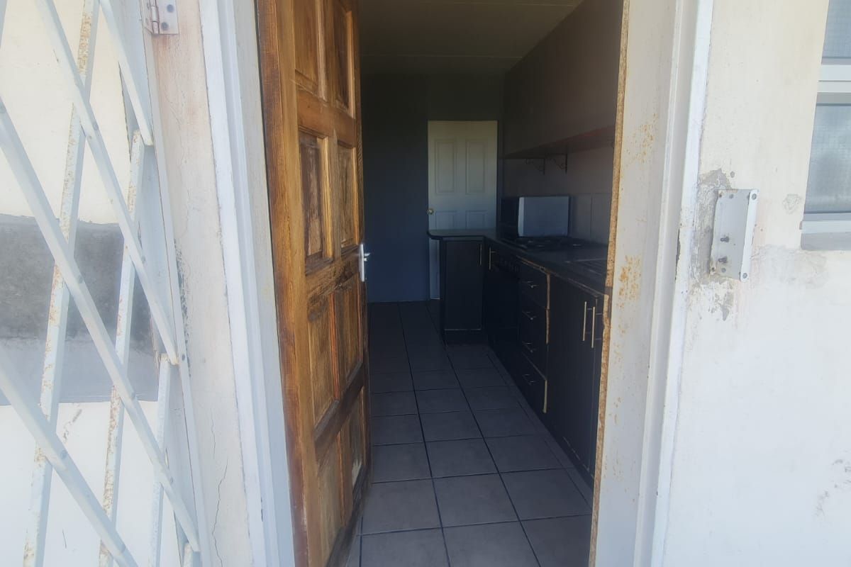 View through an open wooden door into a galley-style kitchen featuring tiled flooring and dark cabinetry.
