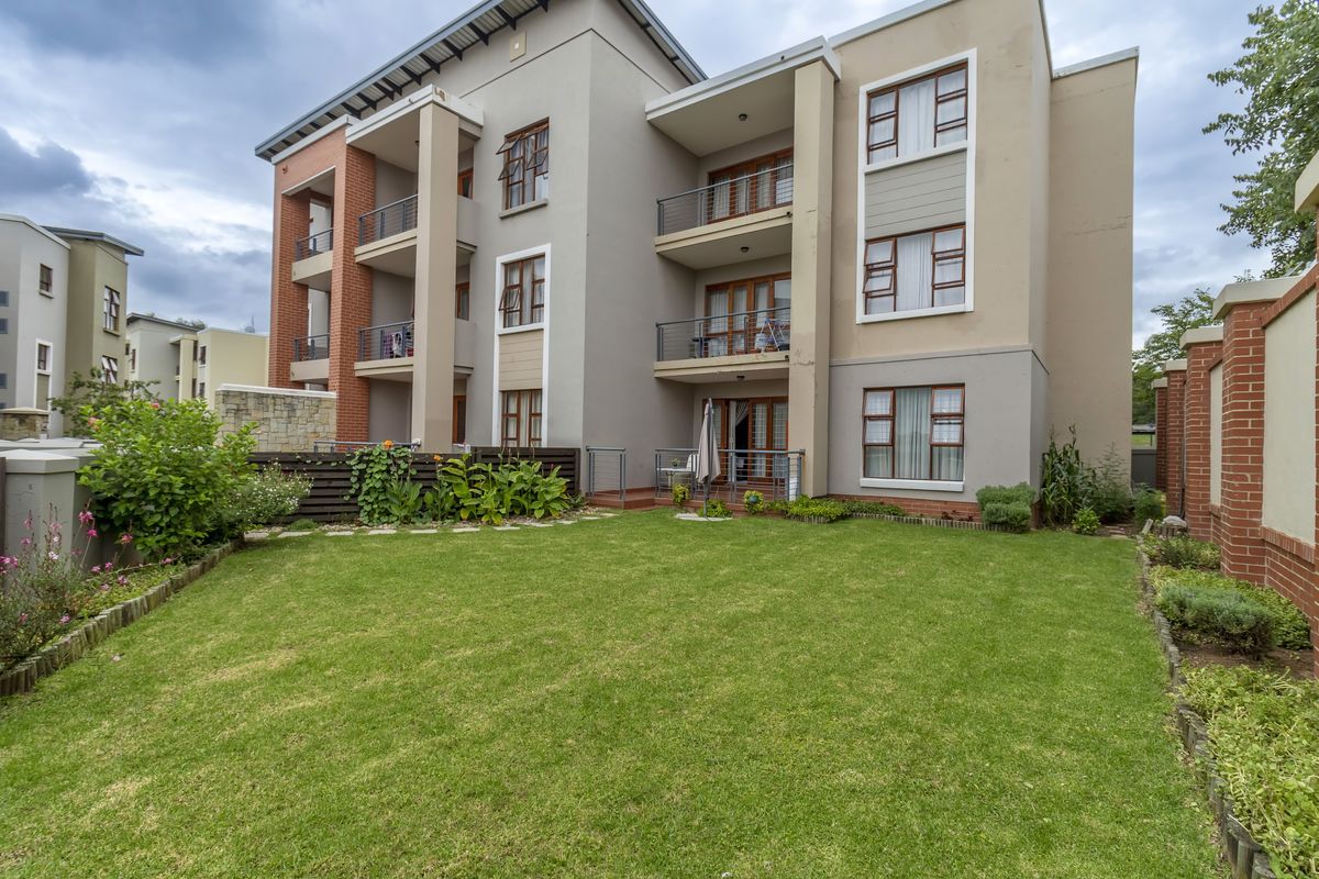 Rear view of a modern apartment complex featuring private balconies, sliding glass doors, and a well-maintained communal lawn area.