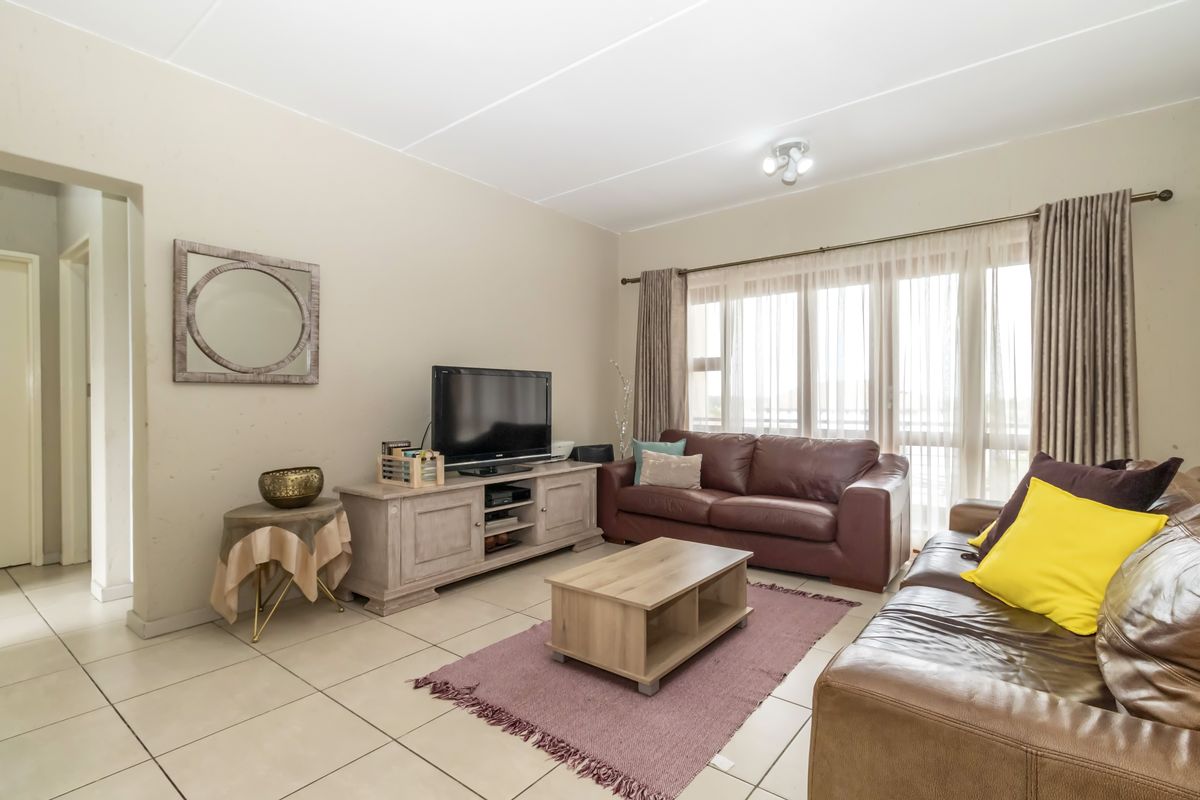 A functional living room featuring neutral tiled flooring, large windows with curtain tracks, and a standard ceiling light fixture.