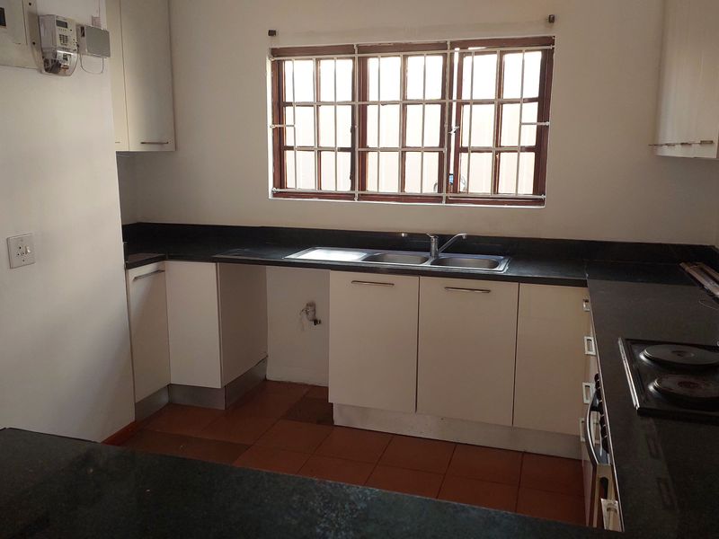 A functional kitchen featuring built-in cabinetry, a double sink, and an electric hob, with security bars on the window and tiled flooring.
